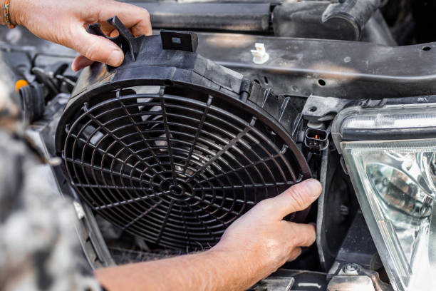 A man inserts an engine cooling fan under the radiator grill of a car for appliance installation and maintenance services in Miami, FL. Machine maintenance and repair.