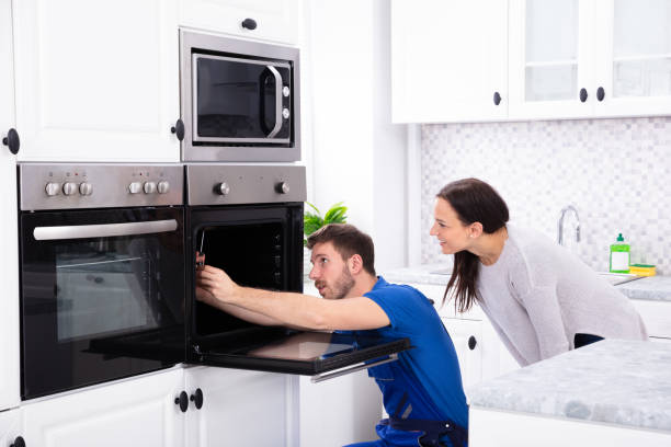 Smiling woman observing a technician fixing an oven in her kitchen, receiving expert appliance installation services in Plantation, FL.