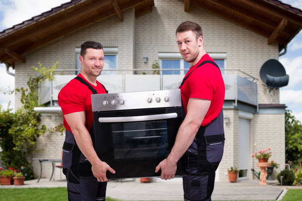 Two men wearing red shirts carefully holding an oven, engaged in the process of appliance installation.