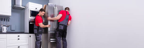 Two men in red shirts work together to install a refrigerator, demonstrating teamwork in appliance installation.