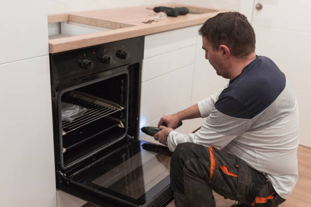 A man repairs an oven in a kitchen, focusing on range and cooktop installation.