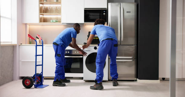 Two men in blue shirts install a refrigerator, focused on their task in a well-lit kitchen environment.