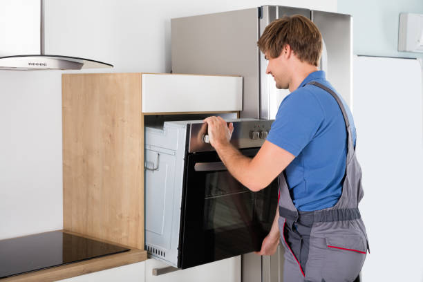 Man wearing overalls opens oven door during wall oven installation, revealing the contents inside.