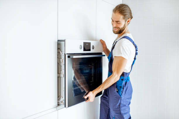 A man in blue overalls opening a wall oven during wall oven installation, likely checking on a dish being cooked.