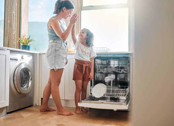 A woman and a child stand in front of a dishwasher, engaged in conversation about installing the appliance.