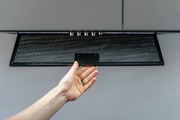 A person reaching up to adjust a black oven vent during a range hood installation process.