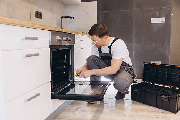 A man in blue overalls stands with an oven, illustrating the process of electric appliance installation.