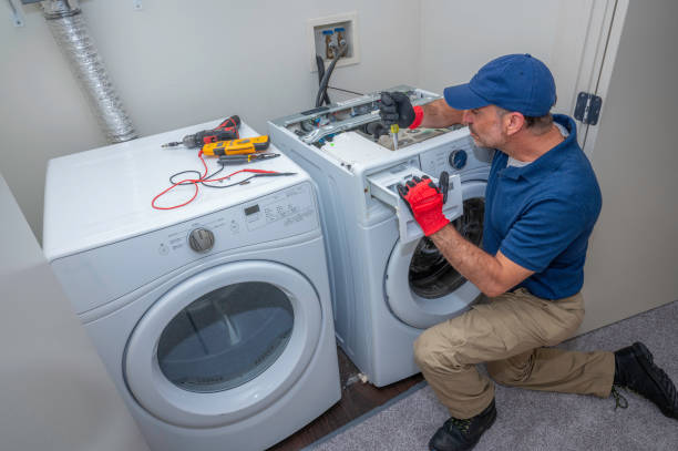 A man wearing blue overalls is holding a washer near dryer, showcasing skills in electric appliance installation.