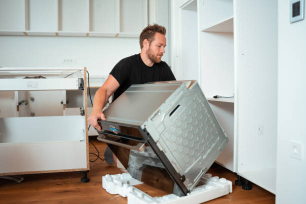 A man in overalls set a oven in wall, focusing on indoor appliance installation and maintenance.