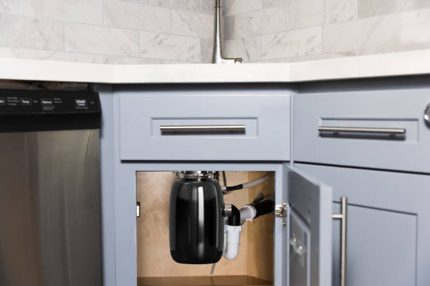 An individual is fixing a water heater beneath a sink, surrounded by tools for garbage disposal installation.