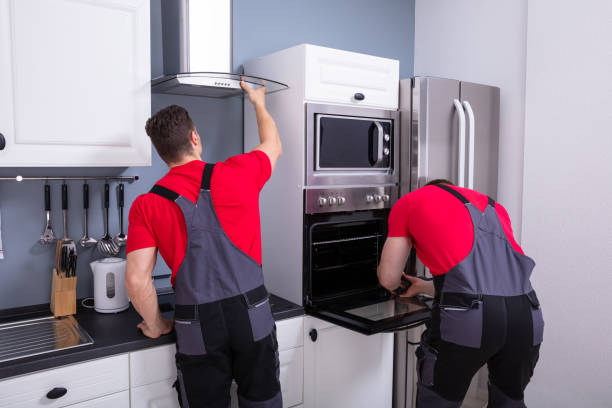Two men in red shirts and overalls installing a cooktop in a kitchen.