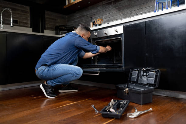 A man repairs an oven in a kitchen, focusing on appliance installation and maintenance tasks.