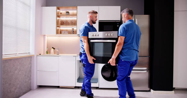 Two men in blue shirts are carefully moving a refrigerator during an appliance installation process.