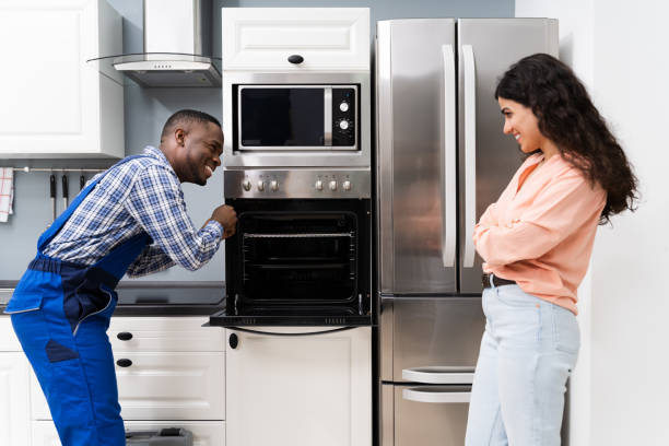 A man and woman stand together in front of an oven, with an over-the-range microwave installed above it.