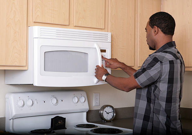 A man and woman pose in front of an oven, featuring an over-the-range microwave mounted above.