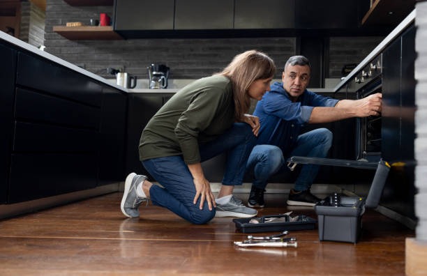 A man and woman collaboratively installing a kitchen appliance, focused on the task at hand in a well-lit kitchen.