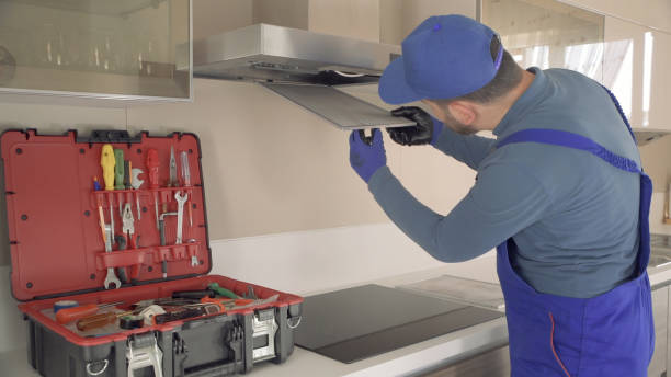 A man in overalls repairs a stove, demonstrating appliance installation skills in a home setting.