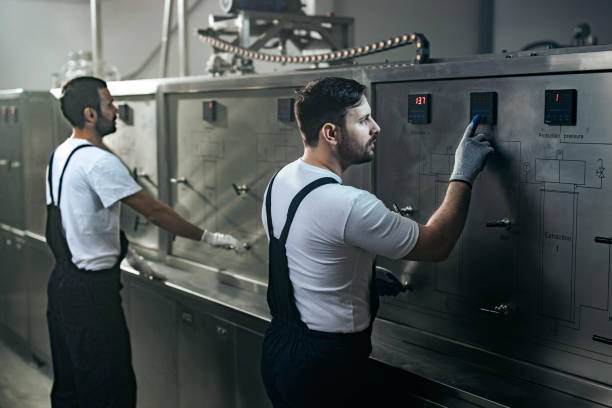 Two men operate a large machine in a factory setting, focused on appliance installation services.