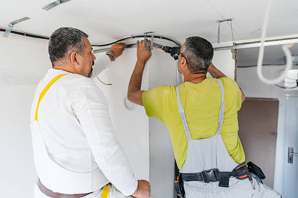 Two men installing electric appliances while working on the ceiling in a room.
