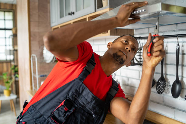 A man wearing overalls is fixing a kitchen sink, emphasizing electric appliance installation.
