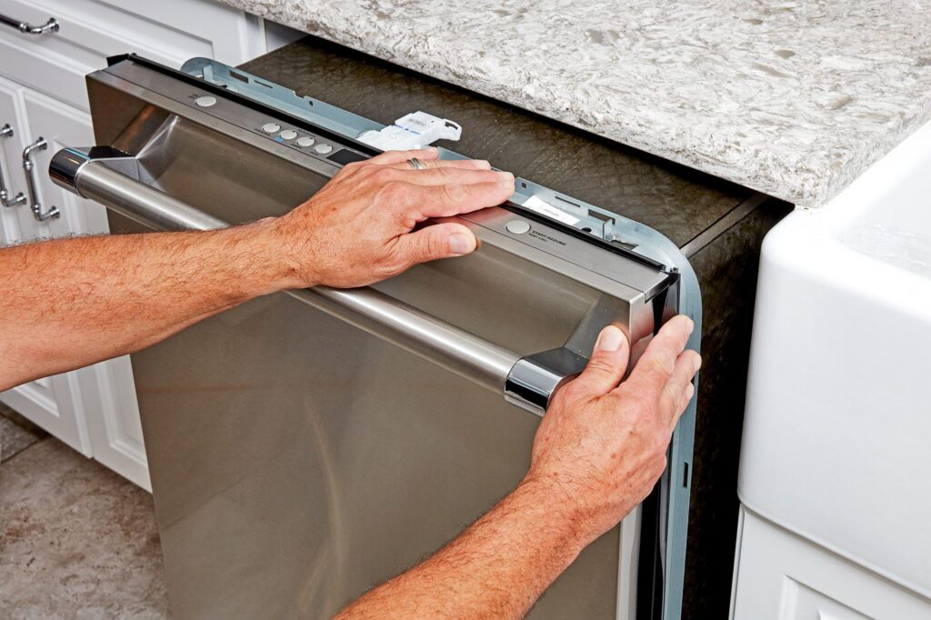 A man is repairing a dishwasher, focusing on the installation process with tools in hand.