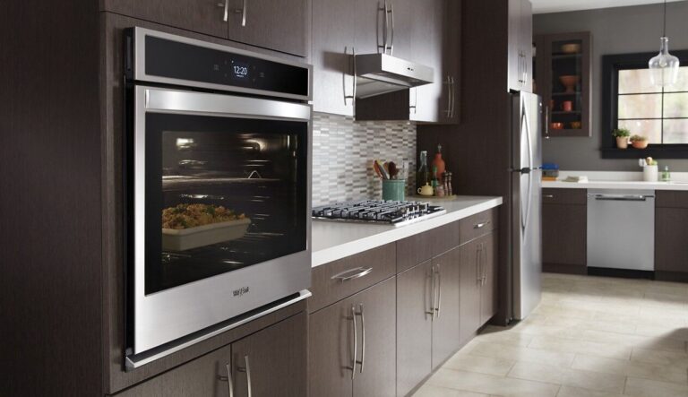 A modern kitchen featuring dark wood cabinetry and stainless steel appliances, highlighting a built-in wall oven with a dish cooking inside.
