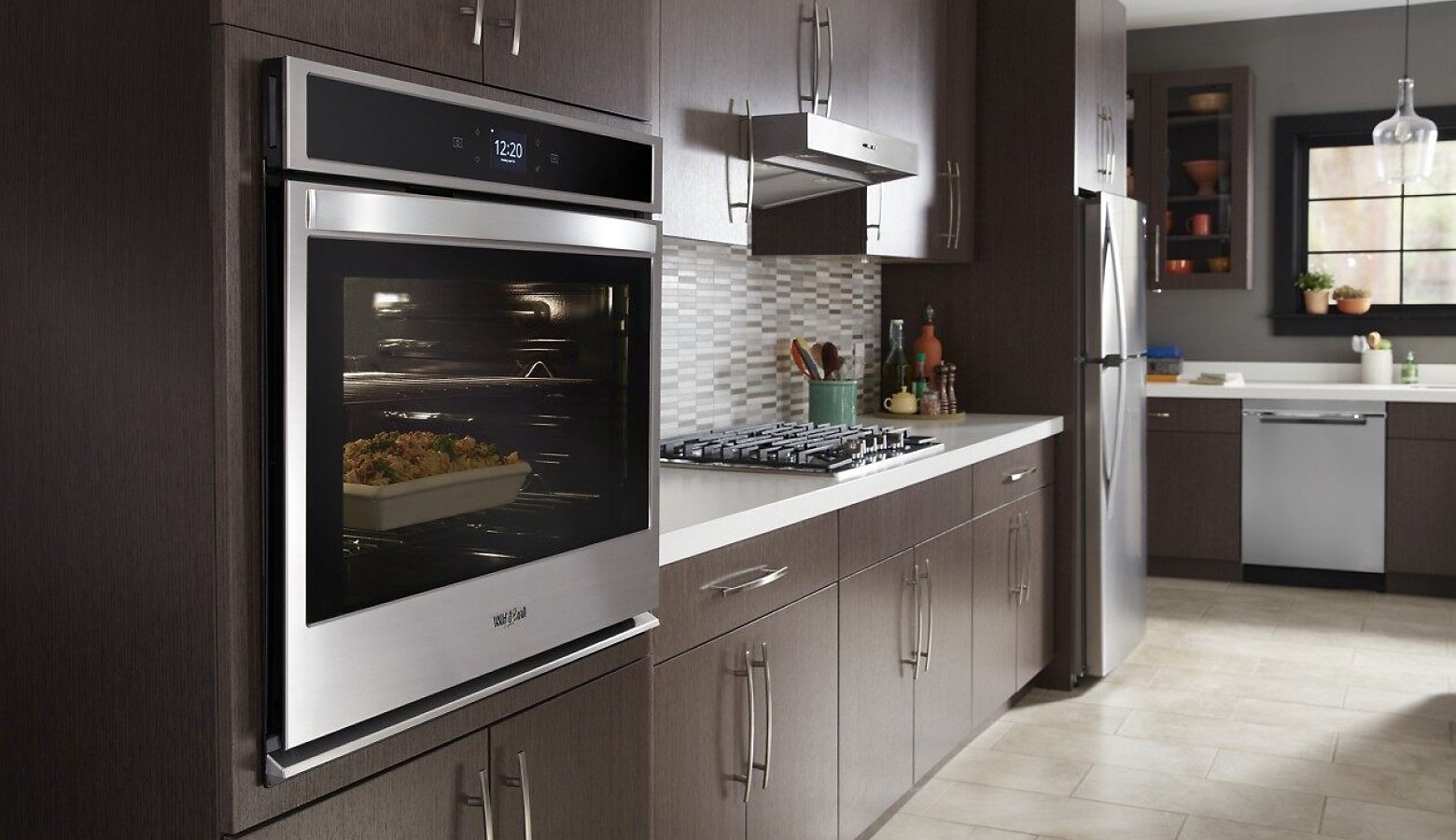 A modern kitchen featuring dark wood cabinetry and stainless steel appliances, highlighting a built-in wall oven with a dish cooking inside.