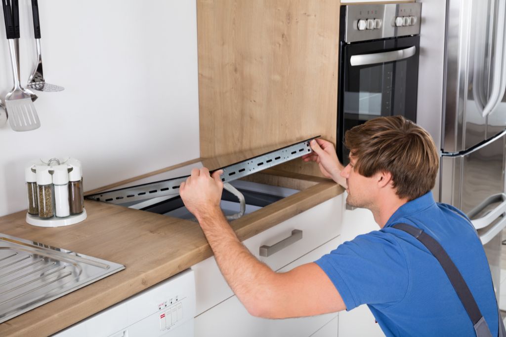A man repairs a sink in a kitchen, focusing on the installation of a new cooktop.