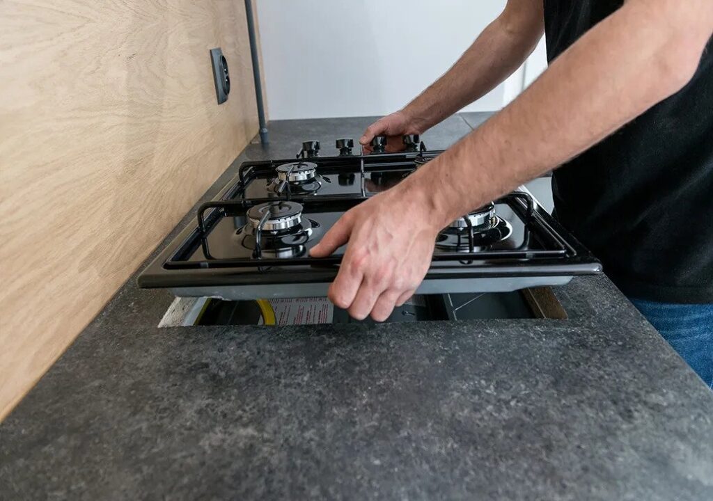 A man installs a gas stove on a kitchen counter as part of the cooktop installation process.