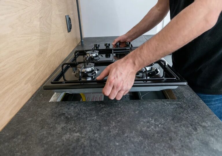 A man installs a gas stove on a kitchen counter as part of the cooktop installation process.